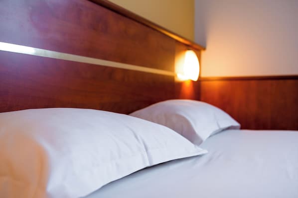 Una habitación de hotel con cabecera de madera y lámpara de pared.