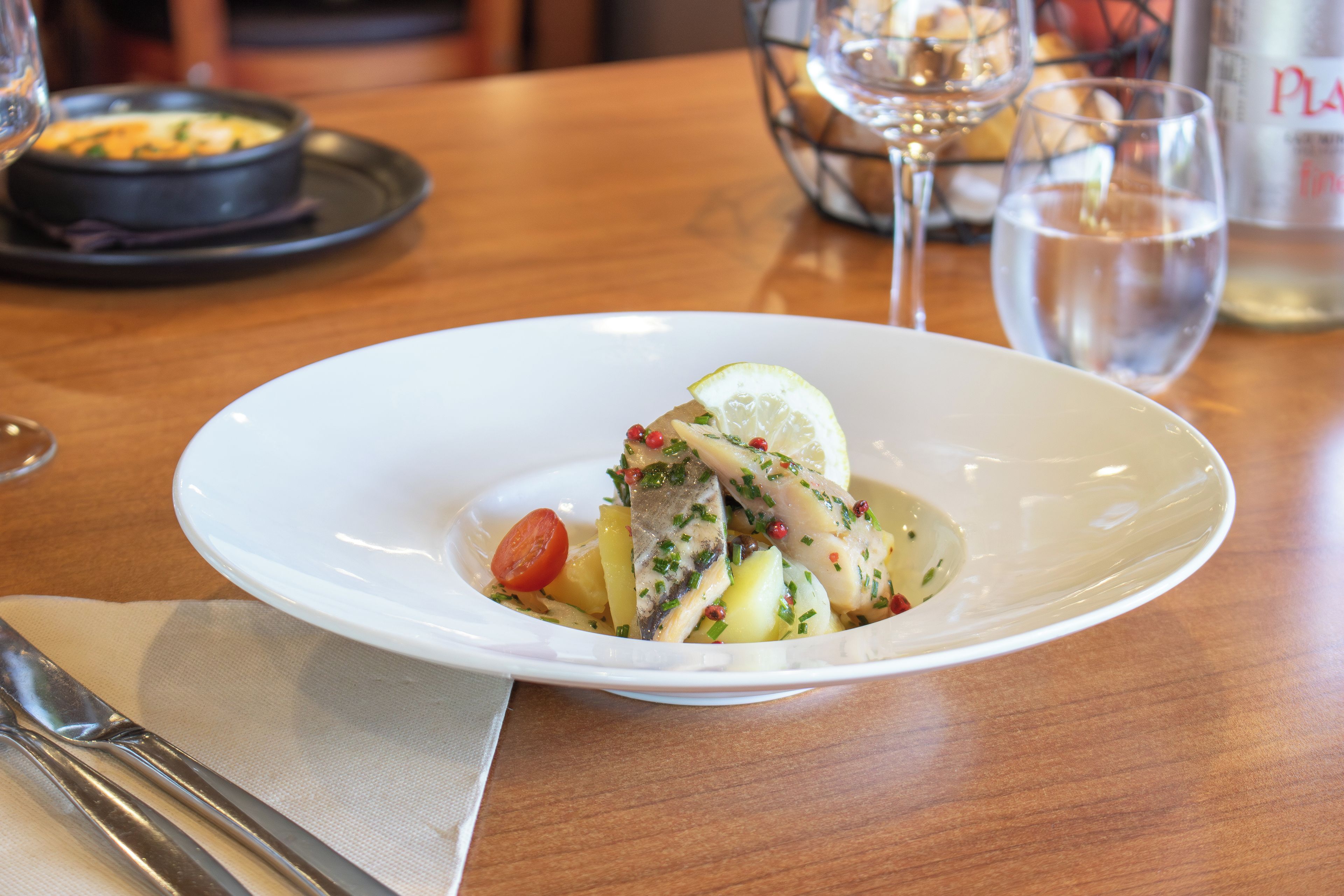 A white plate with a seafood dish, a glass of water, and a glass of wine on a wooden table.