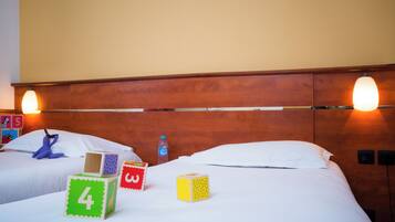 Een hotelkamer met twee bedden, een houten hoofdbord, wandlampen en kinderspeelgoed op de bedden.