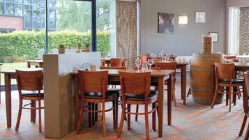 A restaurant with wooden furniture, a bar area, and large windows offering a view of greenery.