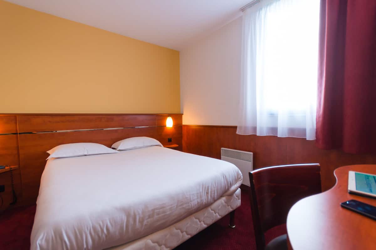 Une chambre d’hôtel avec un grand lit, un bureau et une fenêtre avec des rideaux.