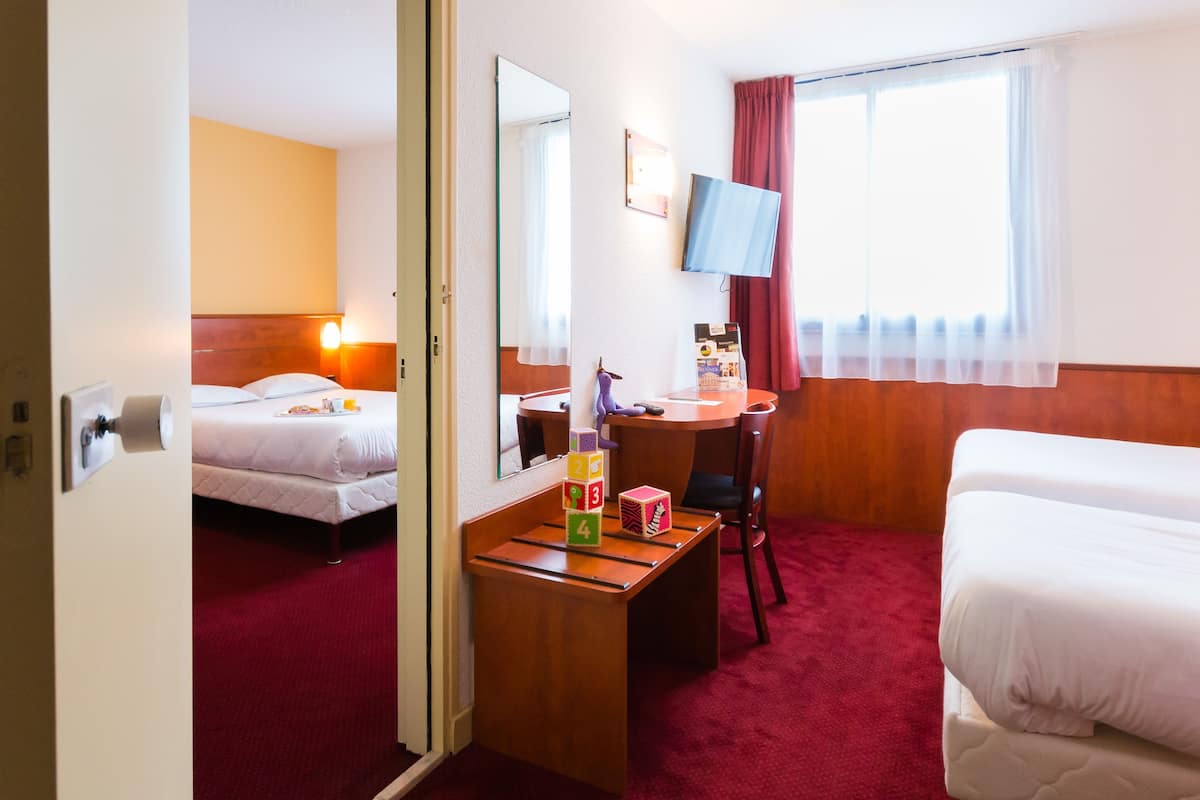 Une chambre d’hôtel avec un lit, un bureau avec un miroir, une télévision et une fenêtre avec des rideaux.