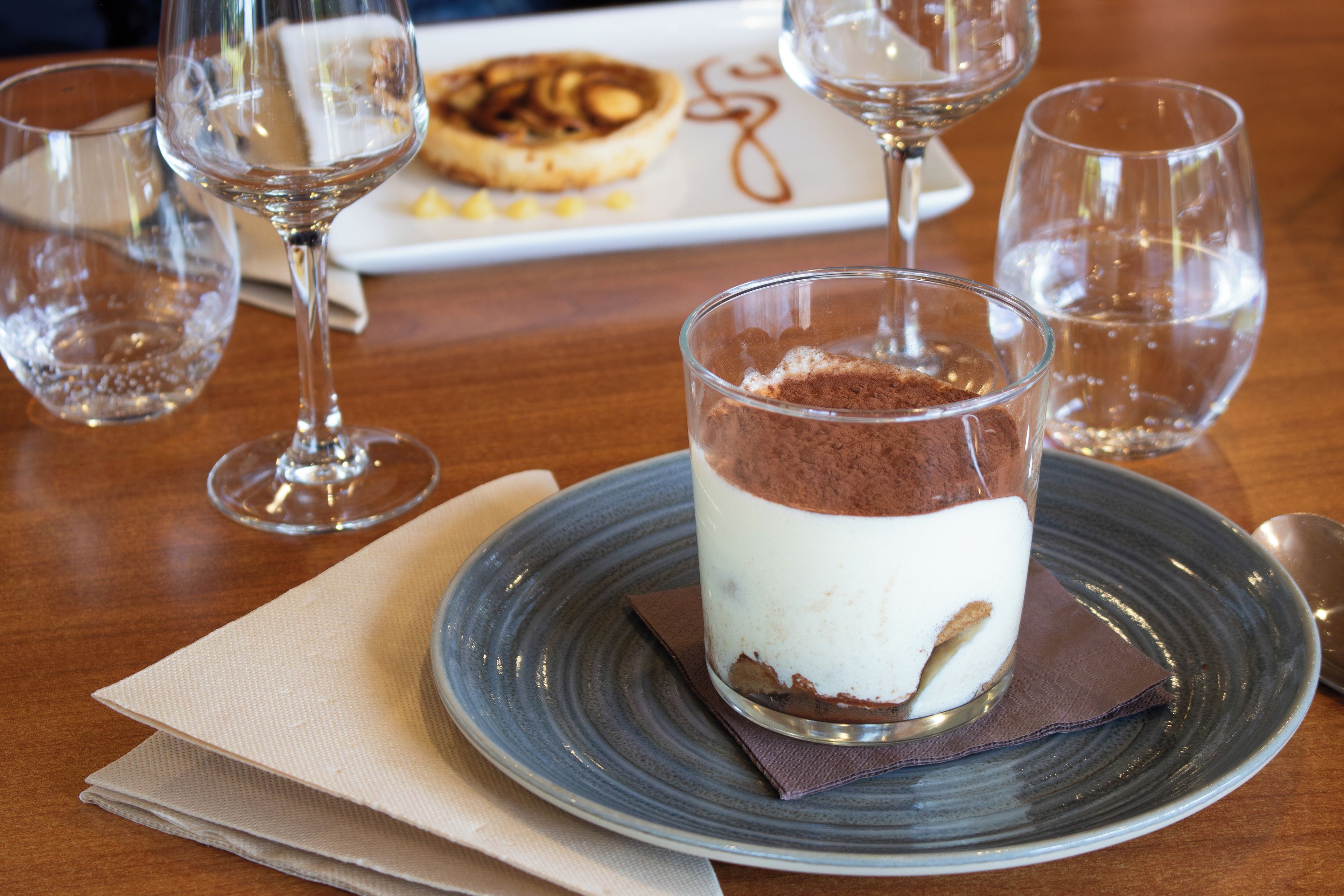 A dessert in a glass on a plate with a napkin and a spoon beside it.
