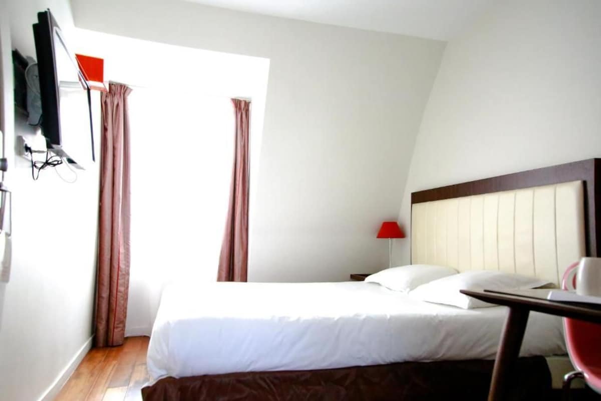 Ein Hotelzimmer mit Bett, Schreibtisch, Stuhl, Wandfernseher und einem fensterbelagten Fenster.