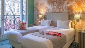 Habitación de hotel con dos camas, un balcón con vistas a edificios y un mural en la pared.