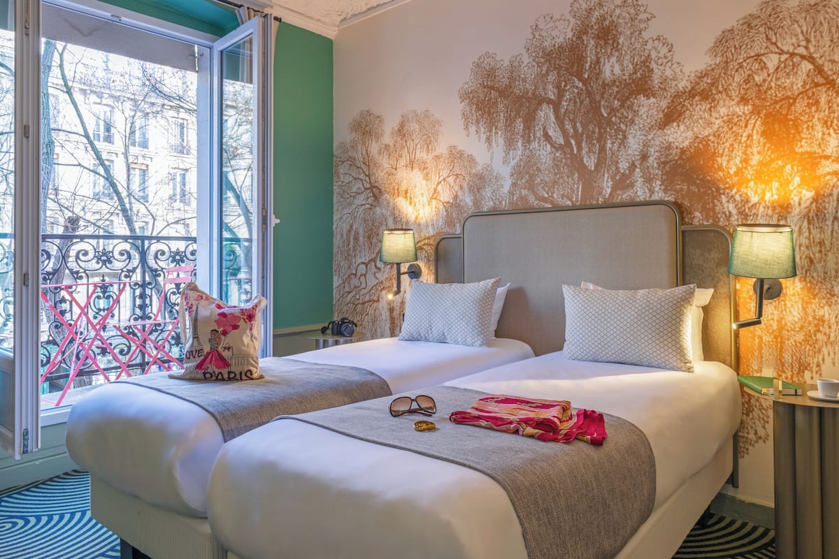Ein Hotelzimmer mit zwei Betten, einem Balkon mit Blick auf Gebäude und einem Wandbild.