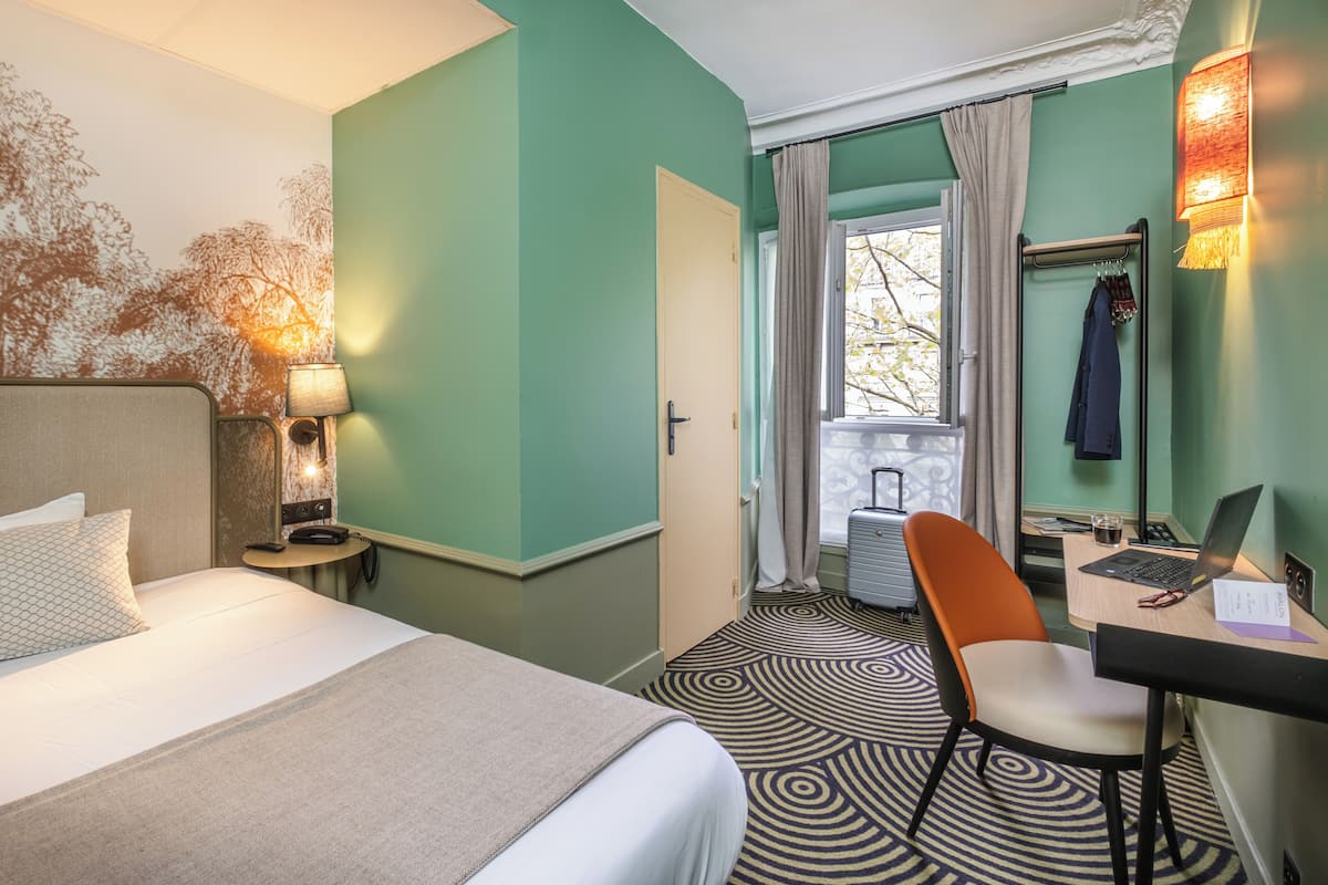Ein Hotelzimmer mit Bett, Schreibtisch, Stuhl, Lampe und Blick ins Freie.