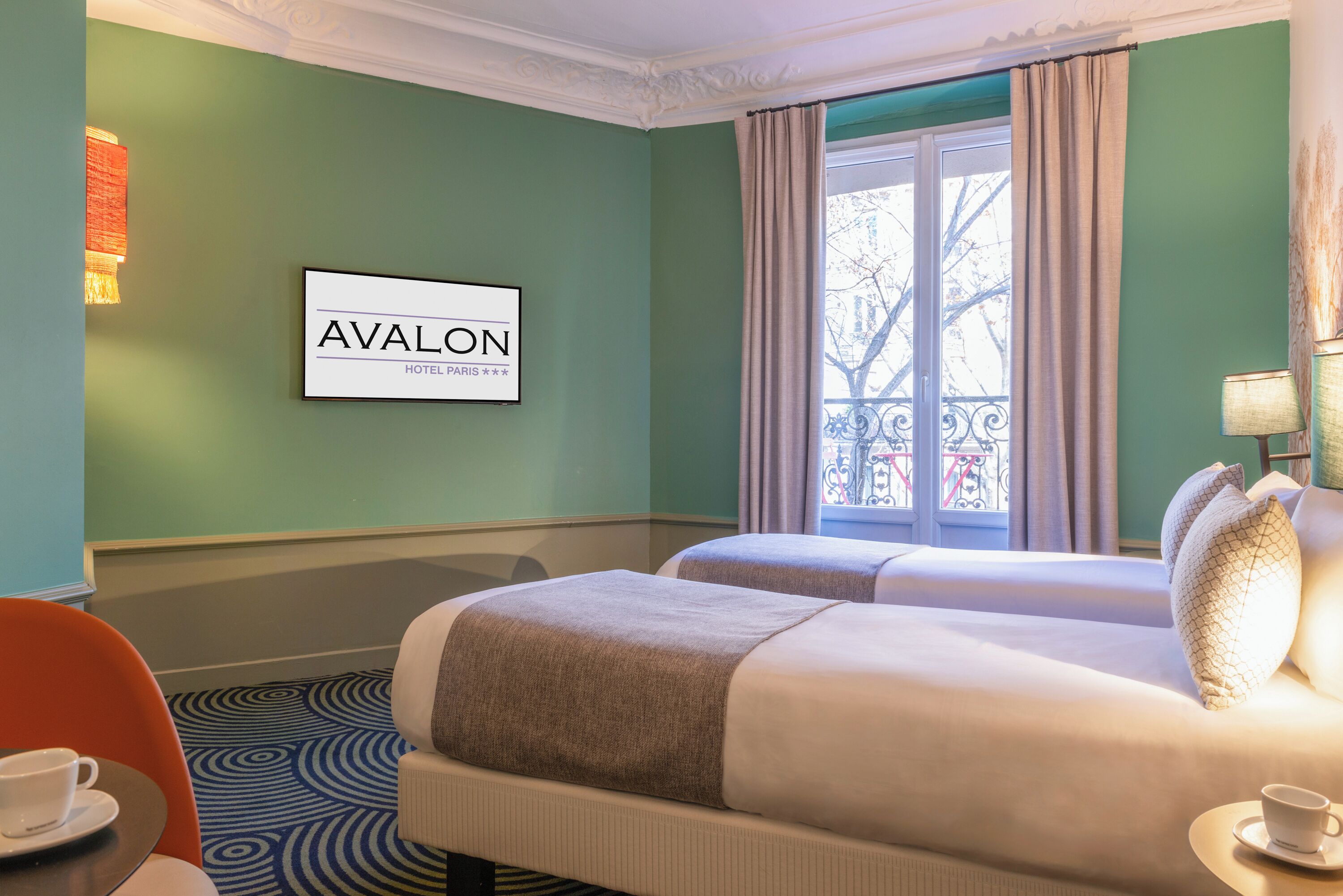Une chambre d’hôtel avec deux lits, un panneau encadré accroché au mur, une fenêtre avec des rideaux et une moquette à motifs.