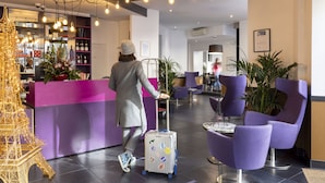 Vestíbulo de hotel con mostrador de recepción, asientos morados y una réplica decorativa de la Torre Eiffel.