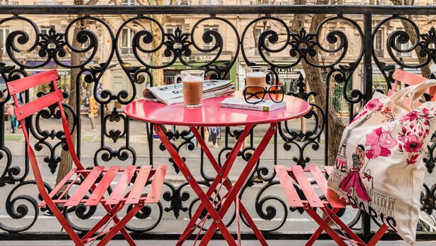 Un área de estar al aire libre con una mesa, sillas, barandilla y árboles de fondo.