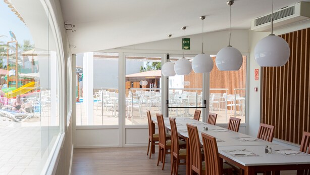 A dining area with a long table, wooden chairs, and hanging pendant lights.