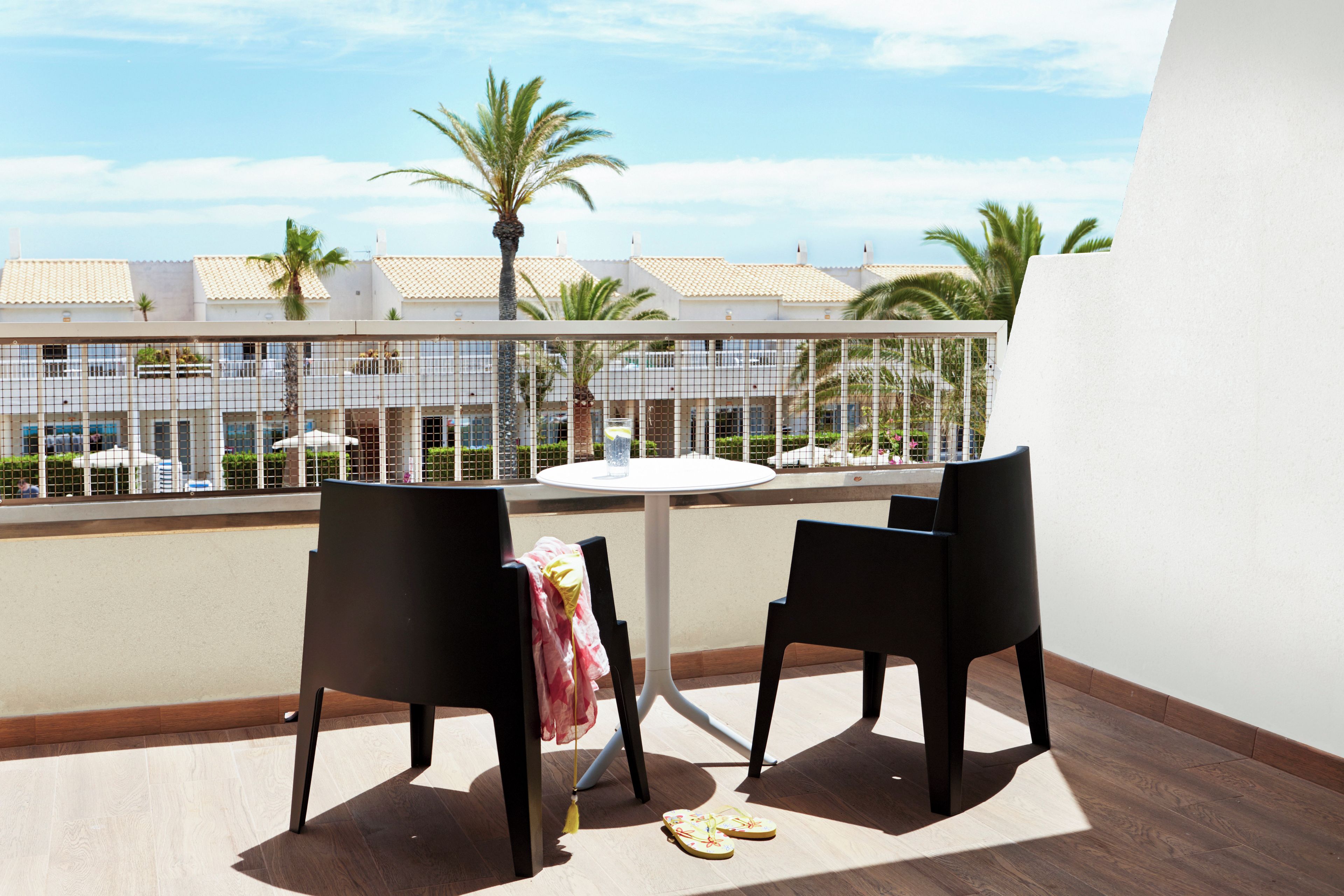 Un balcon avec deux chaises, une petite table ronde et une paire de tongs posées sur le sol.