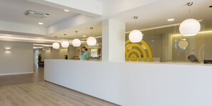 Un área de recepción de diseño moderno, con mostrador de recepción, varias lámparas colgantes y un espejo grande.