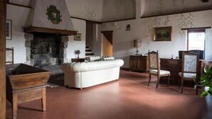 A rustic room with a stone fireplace, a white sofa, wooden furniture, and a staircase leading to an upper level. - Albergo Casalta (Monteriggioni)