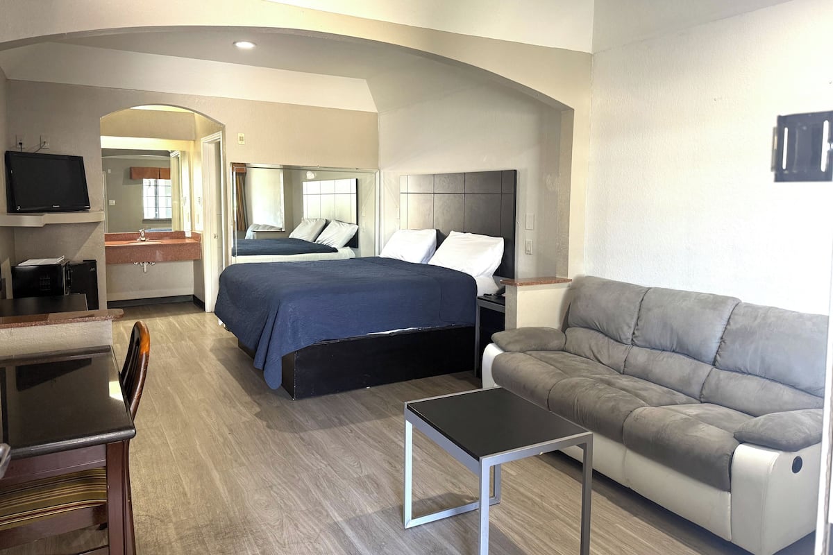 A hotel room with a bed, a sofa, a TV, a desk, and a mirror.