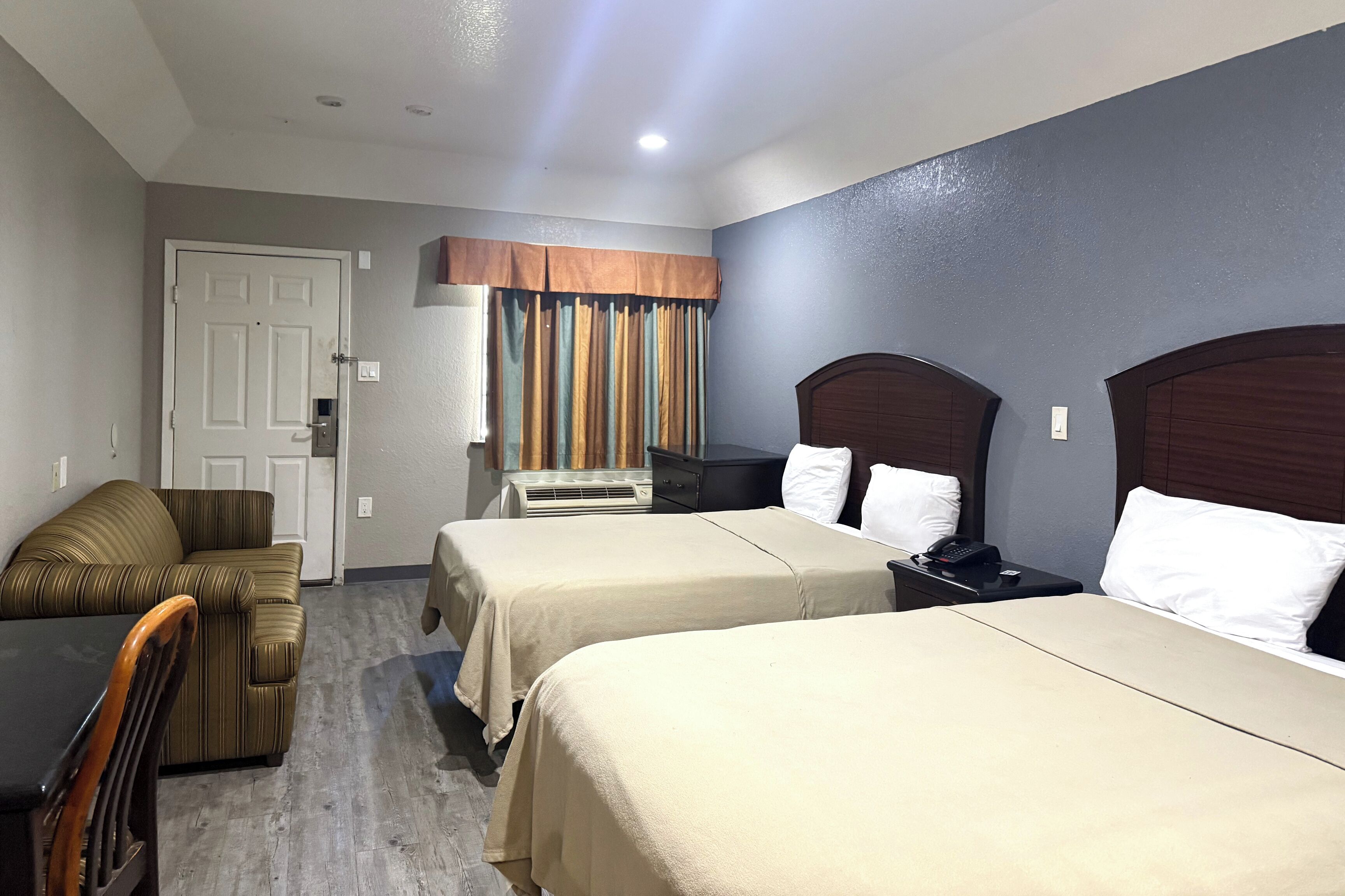 A hotel room with two beds, a sofa, a table, and a desk.