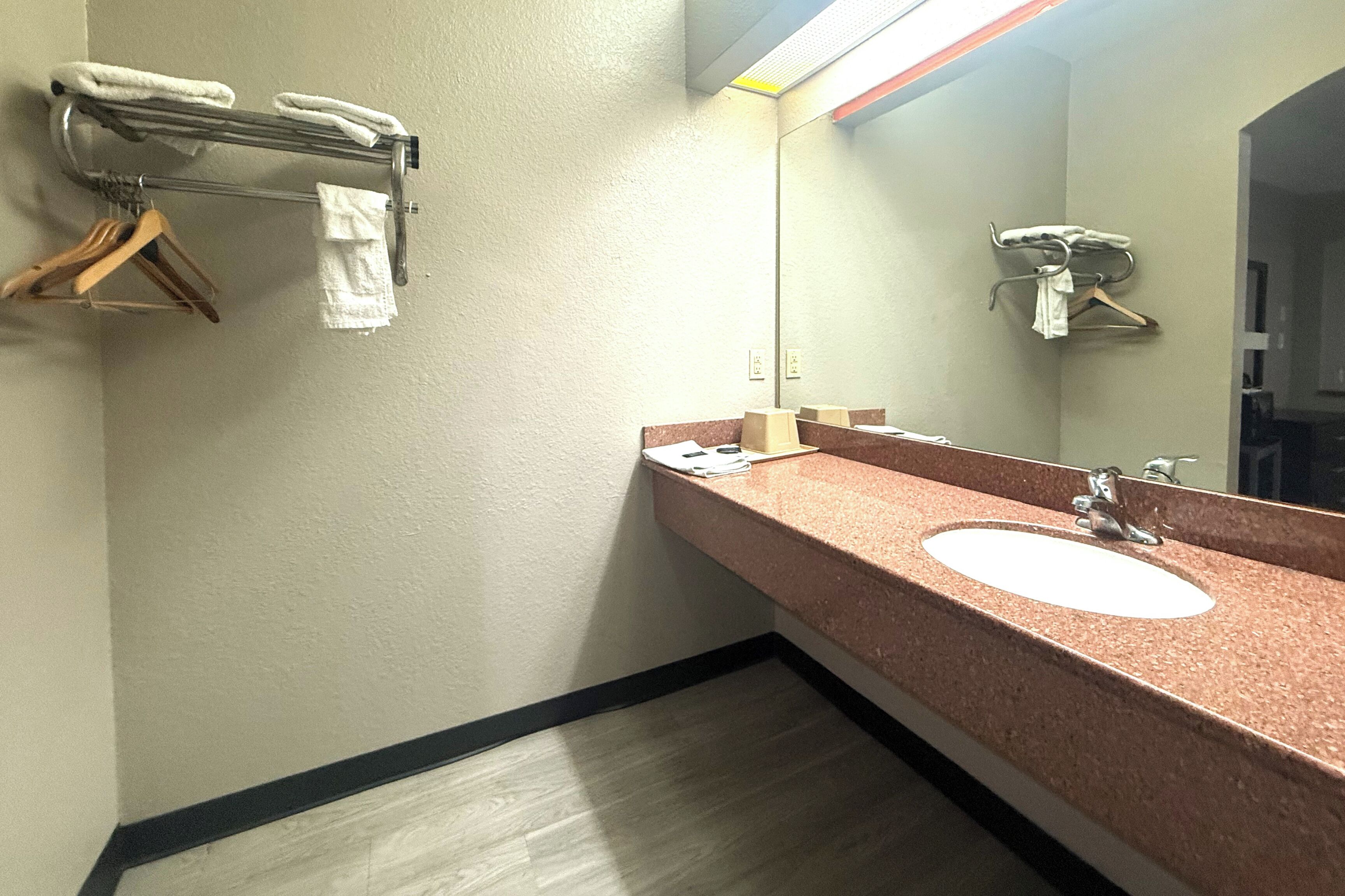 A bathroom with a sink, mirror, towel rack, and wooden hanger.