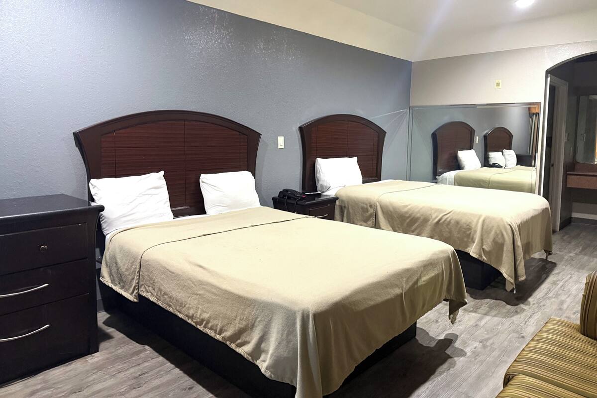 A hotel room with two beds, a dresser, and a chair.