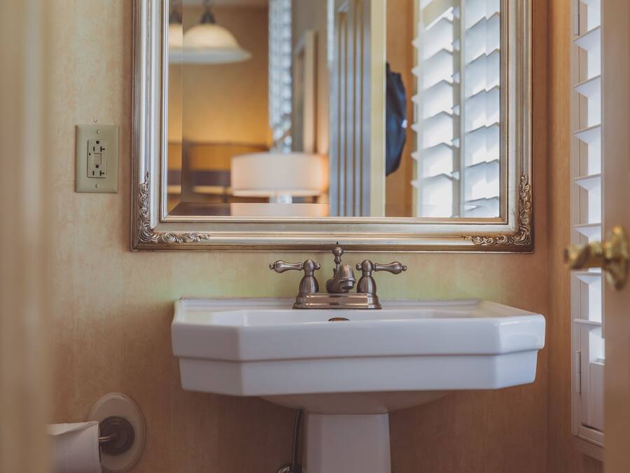 A bathroom with a white sink, a mirror with an ornate frame, and a towel dispenser.