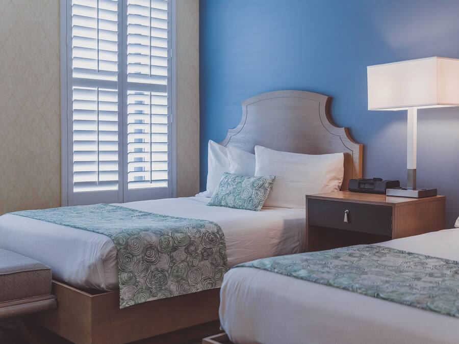 Una habitación de hotel con dos camas, una mesita de noche, una lámpara y una ventana con persianas.