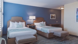 A hotel room with two beds, a bedside table with a lamp, a small cabinet, and a carpeted floor.