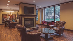 A spacious lobby with a fireplace, leather armchairs, and a large window offering a view of the outdoors.