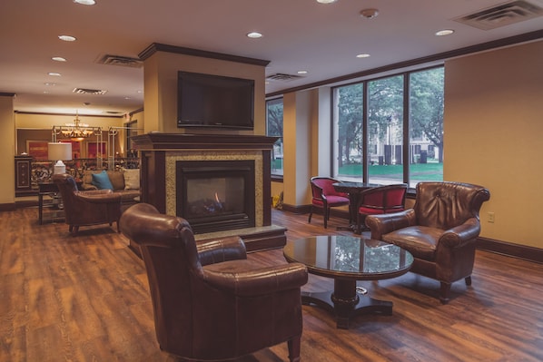 A spacious lobby with a fireplace, leather armchairs, and a large window offering a view of the outdoors.