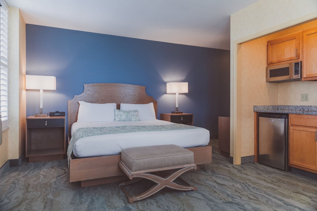 A hotel room with a bed, bedside tables, a lamp, a microwave, and a refrigerator.