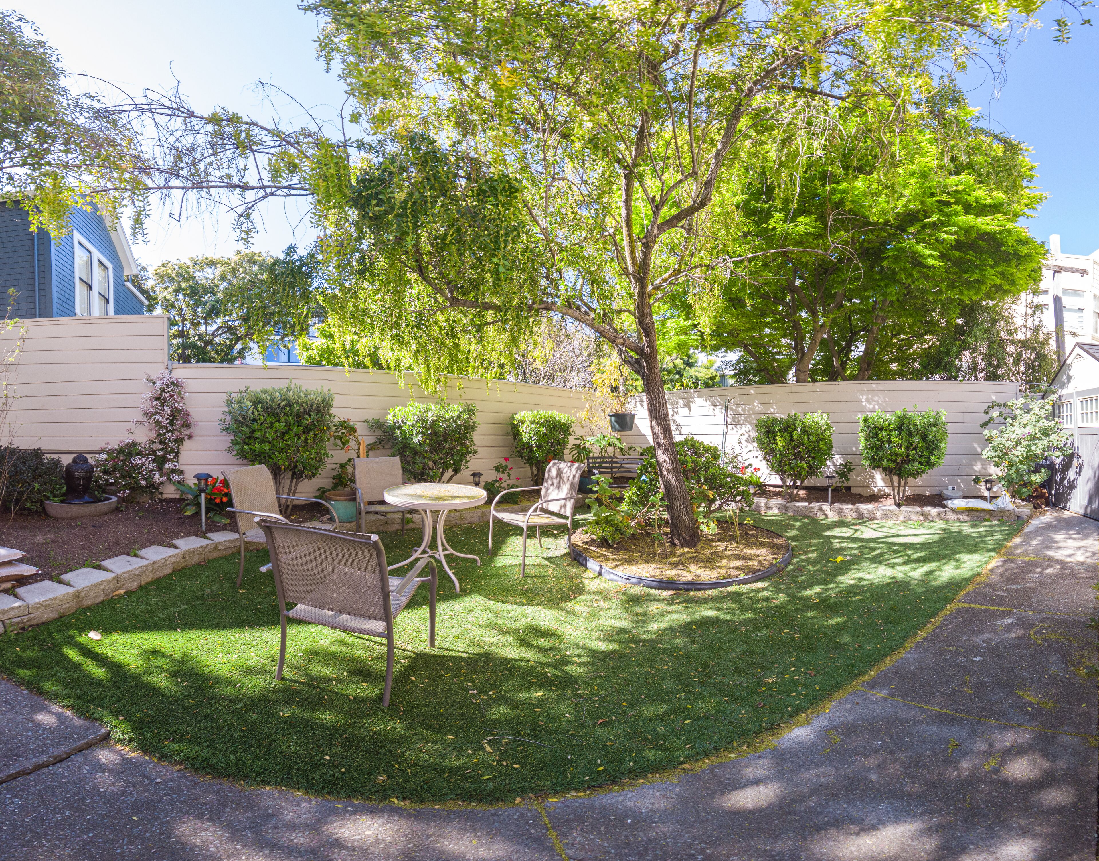 Un jardín cuidado con césped, un árbol pequeño y mobiliario de exterior.