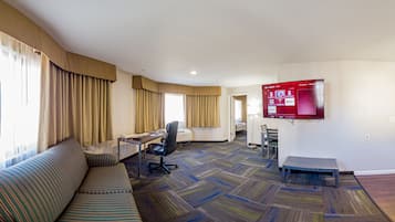Une chambre d’hôtel équipée d’un canapé, d’un bureau, d’une chaise, d’une télévision et dont le sol est recouvert d’une moquette.