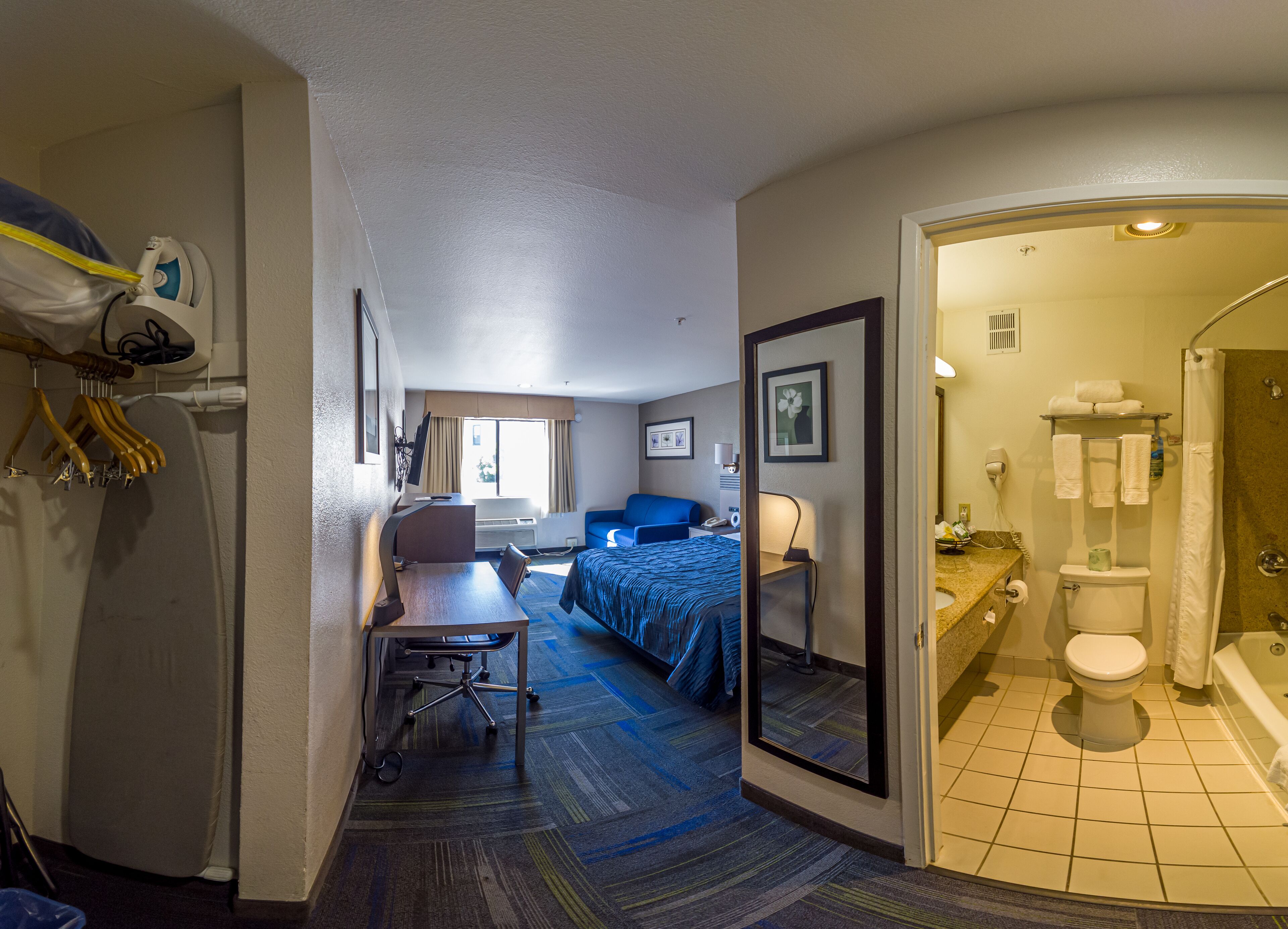A hotel room with a bed, desk, chair, and a bathroom with a shower and toilet.