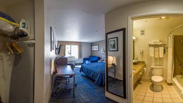 A hotel room with a bed, desk, chair, and a bathroom with a shower and toilet.