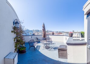 A rooftop patio with a table and chairs, a trash bin, a potted plant, and a view of the city skyline. - Buena Vista Motor Inn (San Francisco)