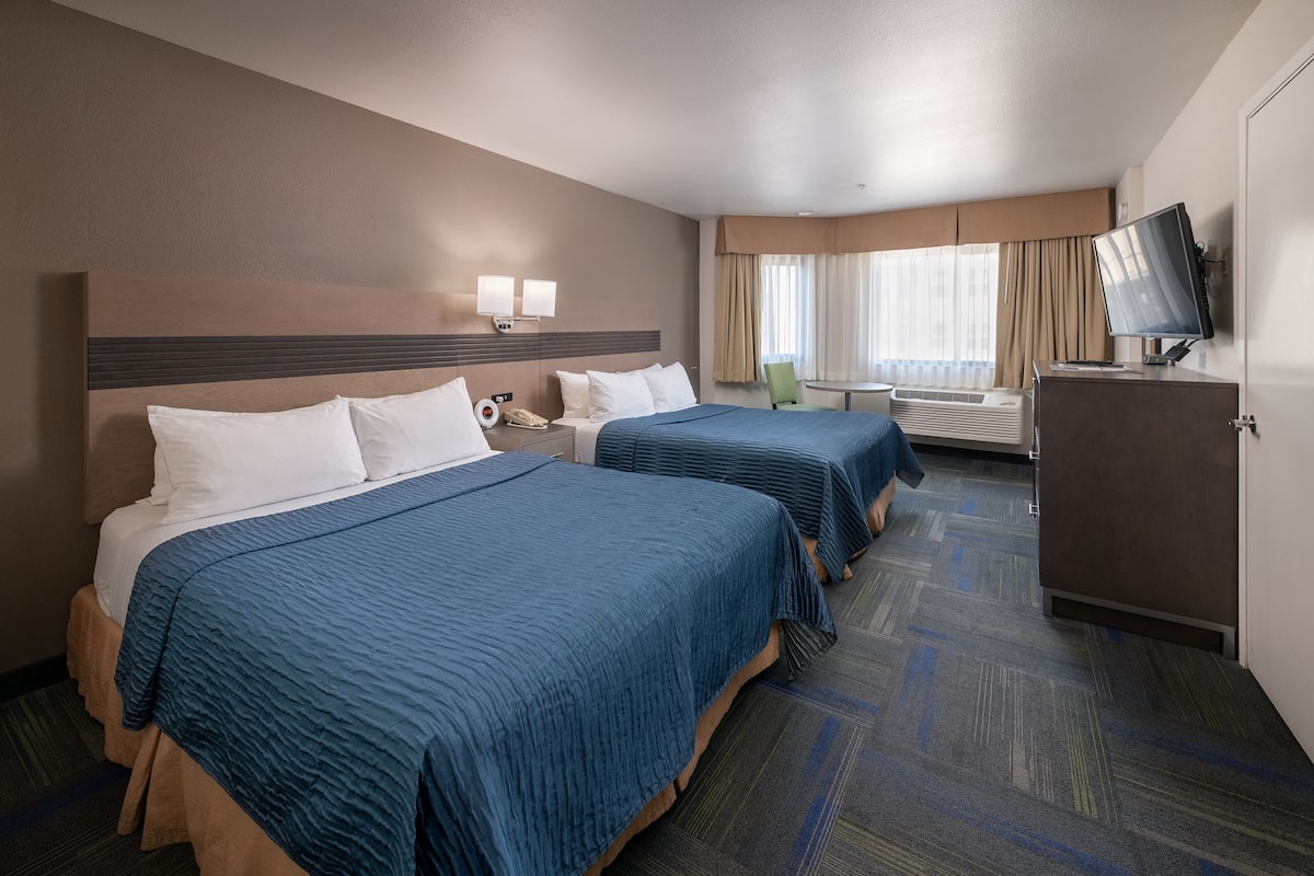 Une chambre d’hôtel avec deux lits, un bureau, une chaise, une télévision et un mini-bar.