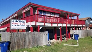 A two-story building with a red and white facade, labeled as the Anchor Motel. It features balconies, a wooden fence, and a signboard with contact information. - Anchor Motel & RV Park (Freeport)