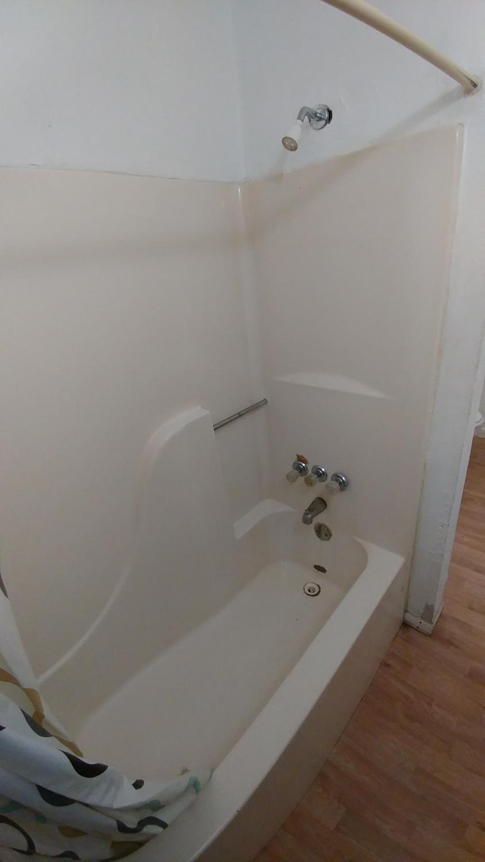 Eine kleine, weiße Eckbadewanne mit Duschkopf, Wasserhahn, Handtuchhalter und Abfluss.