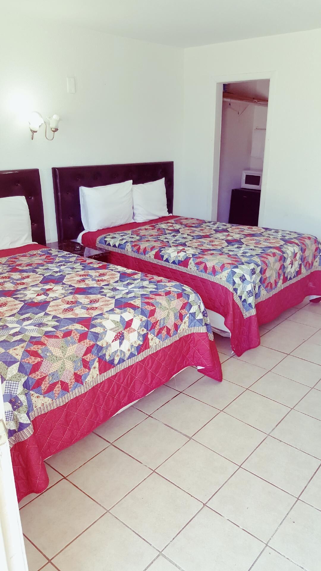 Two twin beds with red and blue quilts, white pillows, and a tiled floor.