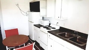 A compact kitchen with a stove, microwave, and sink. There is a red chair and a small table. - Anchor Motel & RV Park (Freeport)