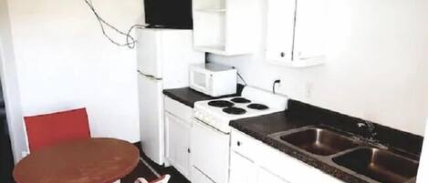 A compact kitchen with a stove, microwave, and sink. There is a red chair and a small table.