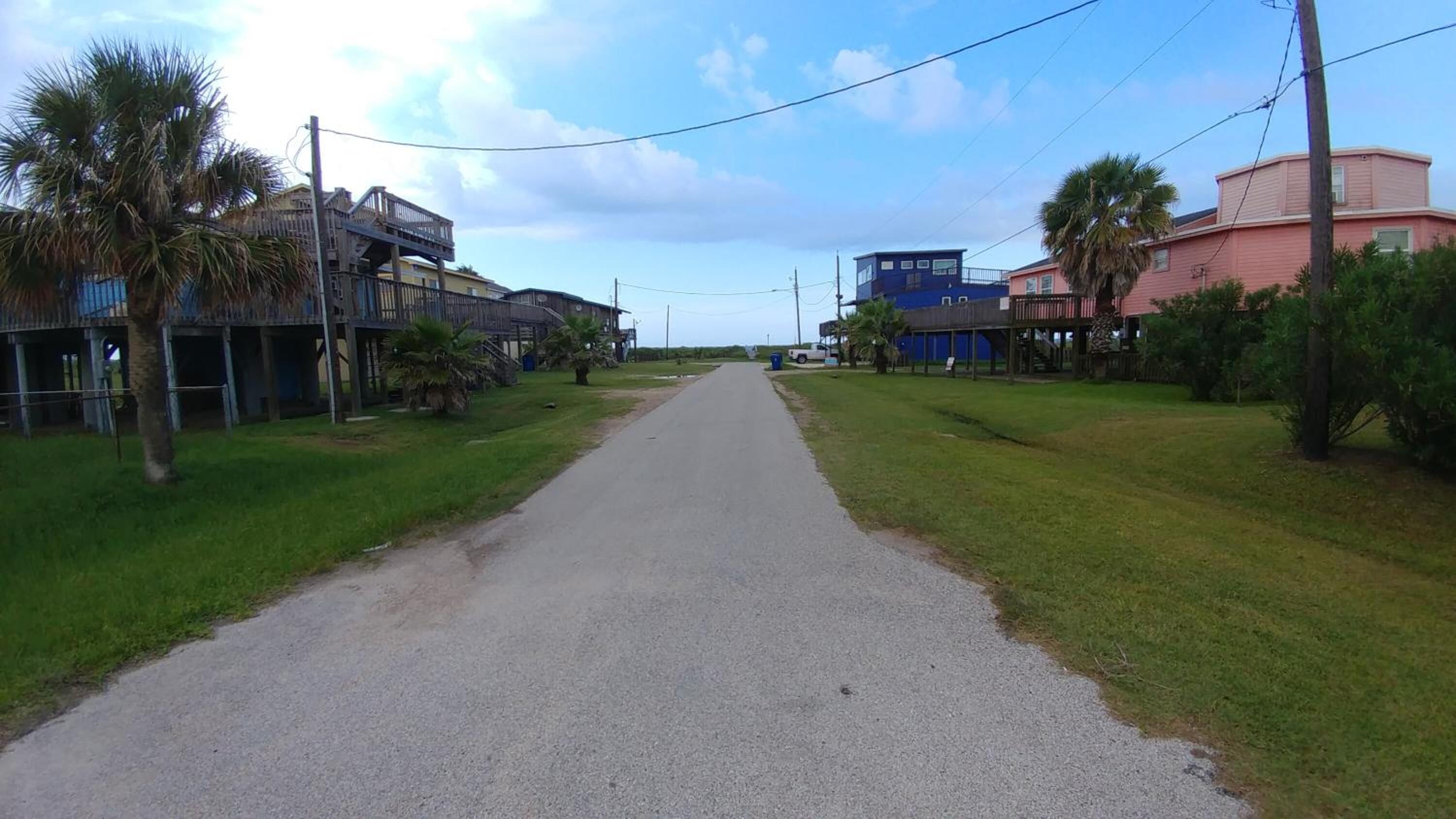 A narrow paved road flanked by residential buildings with flat roofs and minimal landscaping.