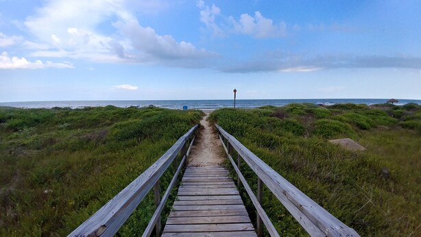 A wooden boardwalk leading to the beach, surrounded by dense vegetation. - Anchor Motel & RV Park (Freeport)