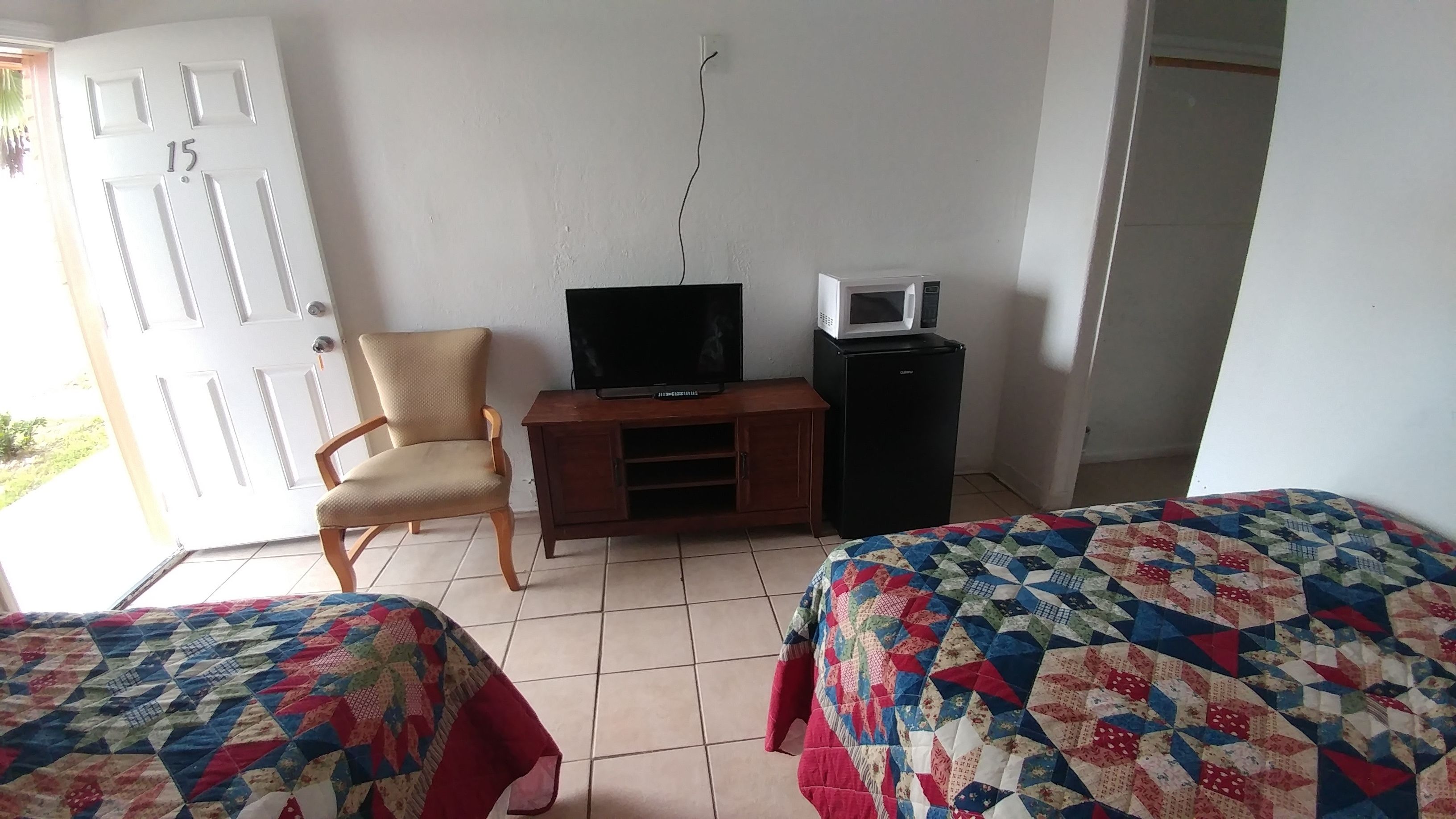 A room with two beds, a TV, a microwave, a small cabinet, and a chair.