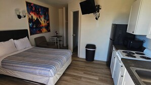 A bedroom with a bed, a painting, a TV, a small table, and a kitchen area with a stove and cabinets. - Anchor Motel & RV Park (Freeport)