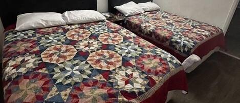 A room with two beds, each with a patterned quilt and white pillows. A painting of a coastal scene is on the wall above the beds.