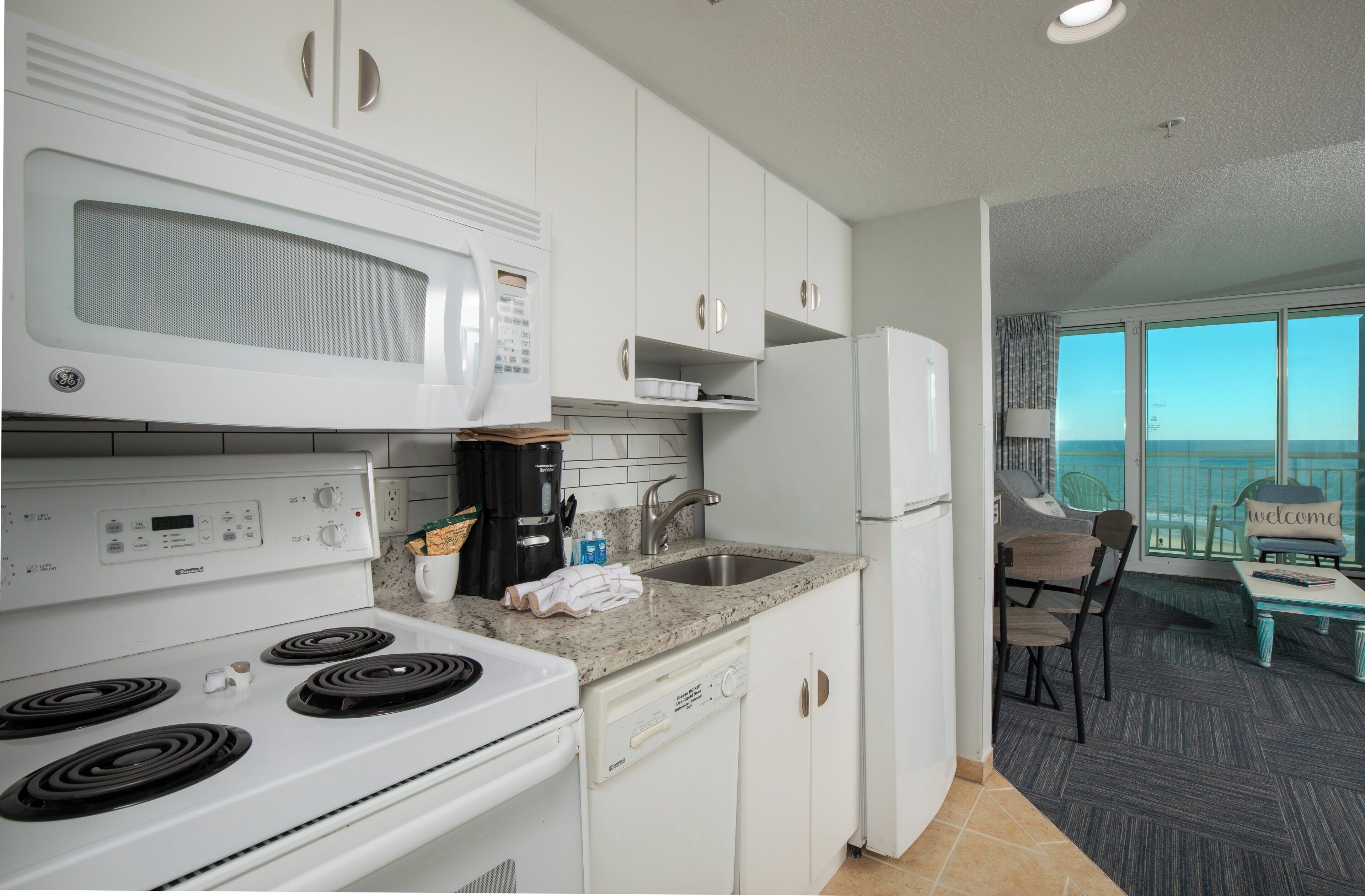 A modern kitchen with white appliances, a dishwasher, and a view of the balcony.