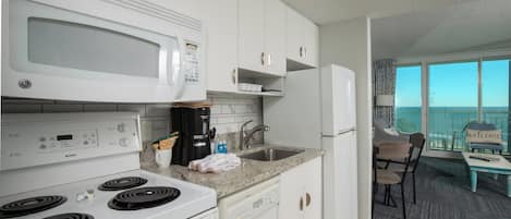 A modern kitchen with white appliances, a dishwasher, and a view of the balcony.