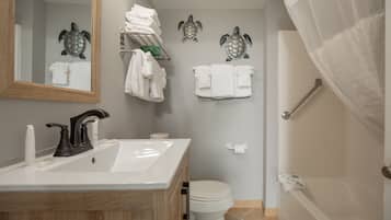 Une salle de bain équipée d’un lavabo, de toilettes et d’une baignoire. On y trouve des serviettes et un rideau de douche.
