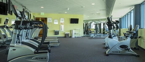 A gym with multiple cardio machines, a television on the wall, and a clear view of the exit.