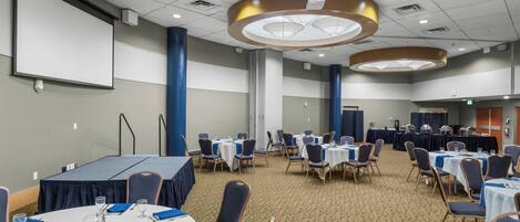 A conference room with round tables, chairs, a projector screen, and a buffet area.