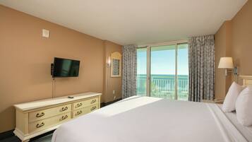 A hotel room with a large bed, a dresser, a television, a balcony with a view, and a lamp.